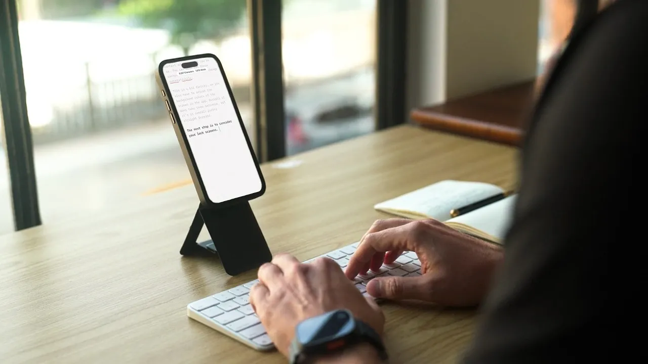 Phone propped on a tripod wallet beside an Apple Keyboard, ready for focused writing with iA Writer.